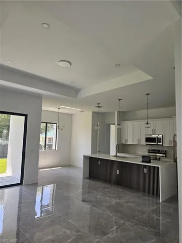 Kitchen featuring hanging light fixtures, white cabinetry, sink, and a tray ceiling