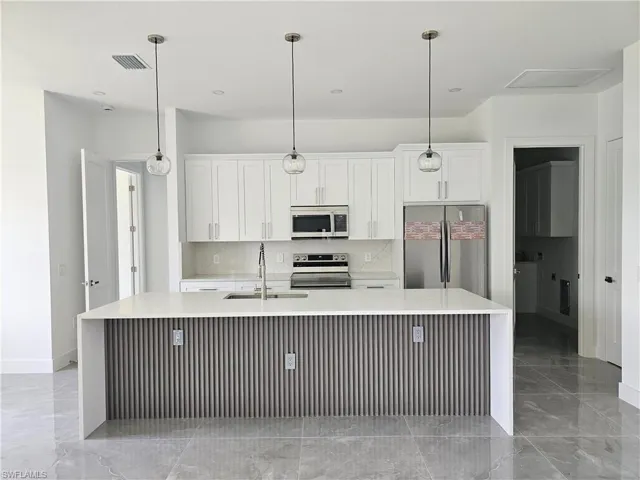 Kitchen with hanging light fixtures, a center island with sink, appliances with stainless steel finishes, and white cabinets