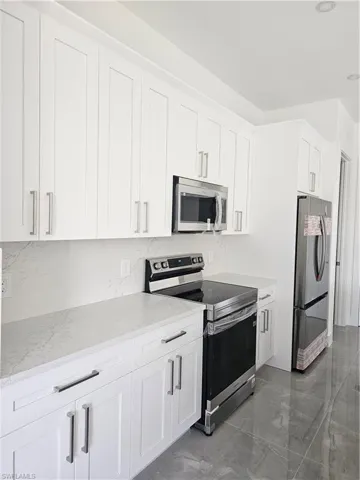 Kitchen featuring light stone counters, tile floors, stainless steel electric stove, refrigerator, and white cabinets