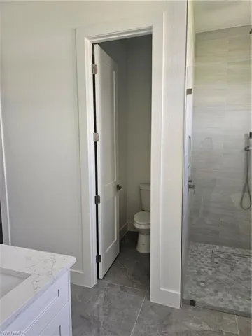 Bathroom with a tile shower, tile flooring, vanity, and toilet