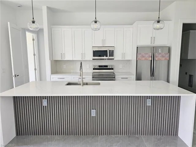 Kitchen featuring light stone countertops, stainless steel appliances, a center island with sink, and backsplash