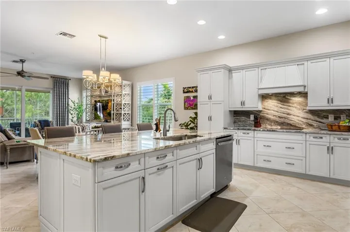 Kitchen with a kitchen island with sink, light stone countertops, suspended lighting, a ceiling fan, and white cabinets
