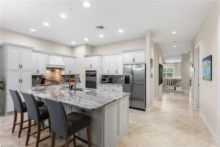 Kitchen featuring stainless steel appliances, light stone countertops, a breakfast bar, recessed lighting, and a kitchen island with sink