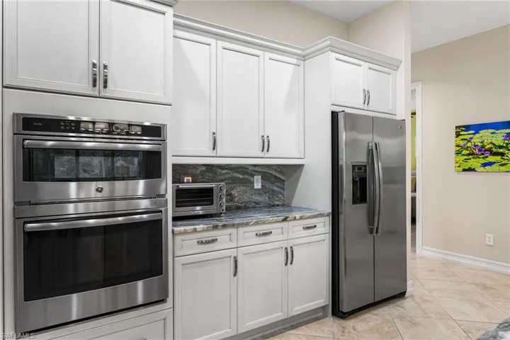 Kitchen featuring stainless steel appliances, dark stone countertops, decorative backsplash, and white cabinetry
