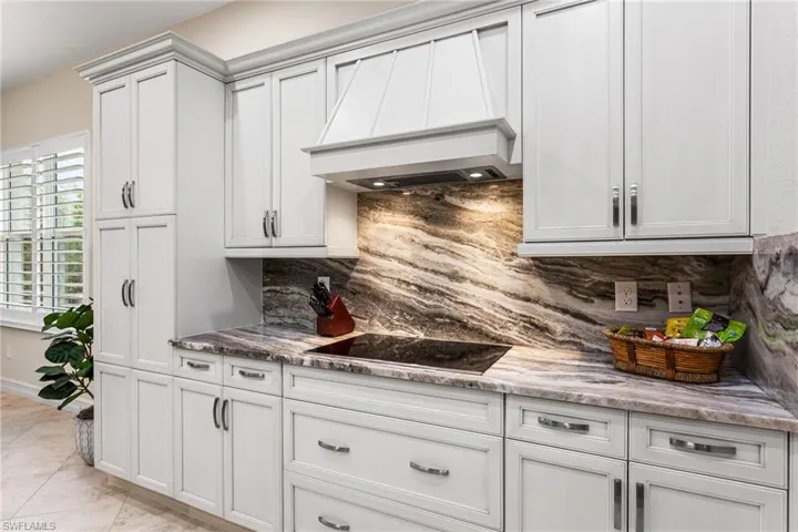 Kitchen with backsplash, light stone counters, black electric stovetop, and white cabinets