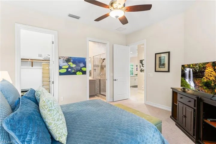 Bedroom with ceiling fan, light colored carpet, a spacious closet, and ensuite bath