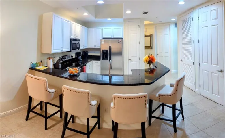 Kitchen with light tile patterned floors, kitchen peninsula, white cabinetry, stainless steel appliances, and a breakfast bar area