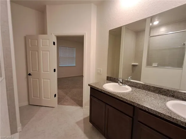 Full bath with double vanity, light tile patterned flooring, and a textured wall