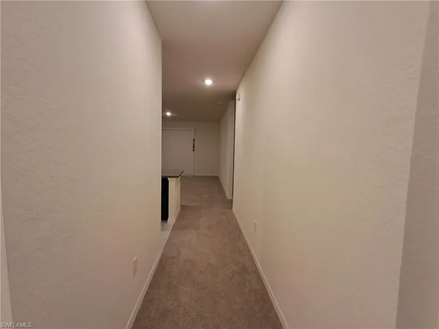 Corridor featuring light colored carpet, a textured wall, and recessed lighting