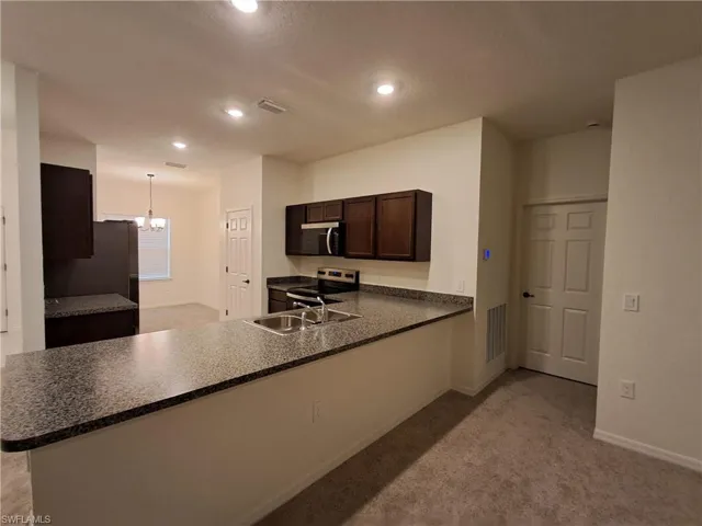Kitchen featuring dark brown cabinetry, a peninsula, dark countertops, light carpet, and a chandelier