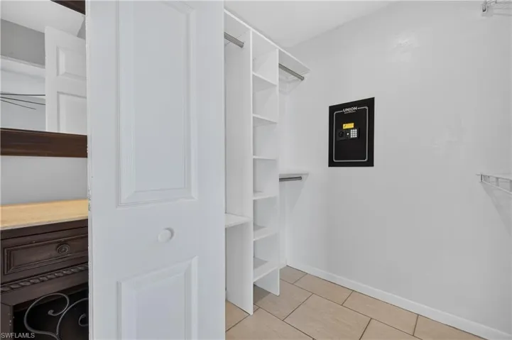 Built-in shelving, hanging rods, and an integrated wall safe within a closet space with tile flooring