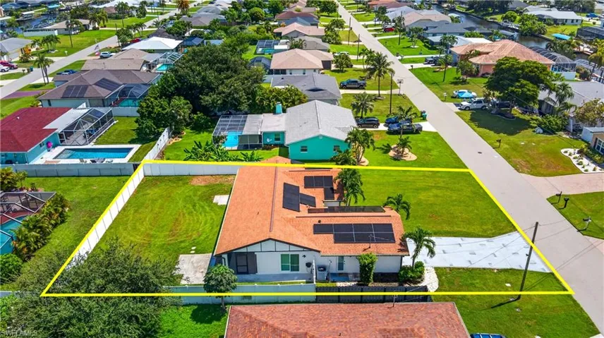 Expansive property featuring a terracotta-style roof, solar panels, mature landscaping, and a patterned driveway
