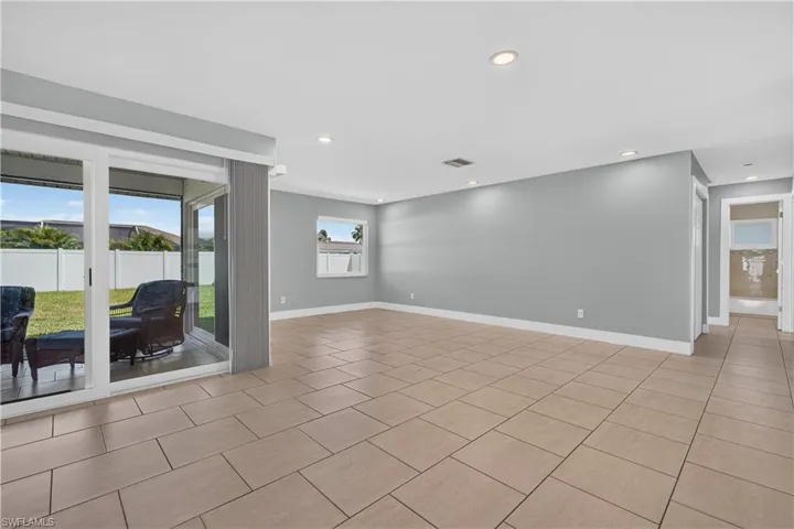 Expansive open-concept room featuring neutral-toned tile flooring, recessed lighting, and sliding glass doors to a covered patio
