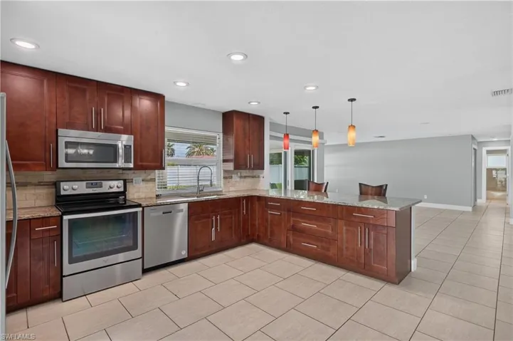 Kitchen featuring wood cabinetry, stainless steel appliances, a center island with pendant lighting, and tile flooring