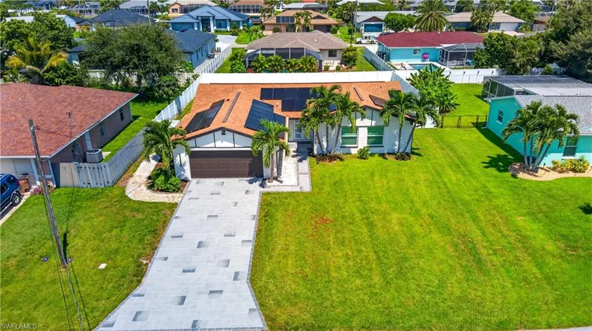 Expansive green lawn surrounds the residence featuring solar panels, a brown shingle roof, attached garage, and a paver driveway