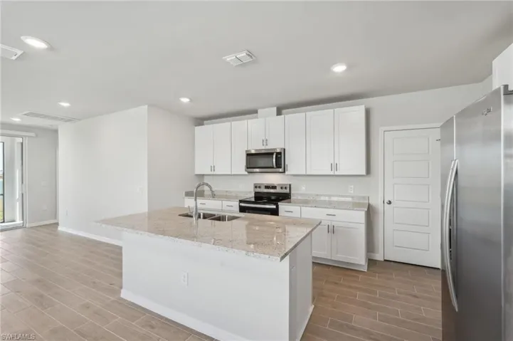 Kitchen with stainless steel appliances, light wood-style floors, visible vents, and a sink