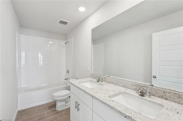 Full bathroom with a sink, visible vents, toilet, and wood tiled floor