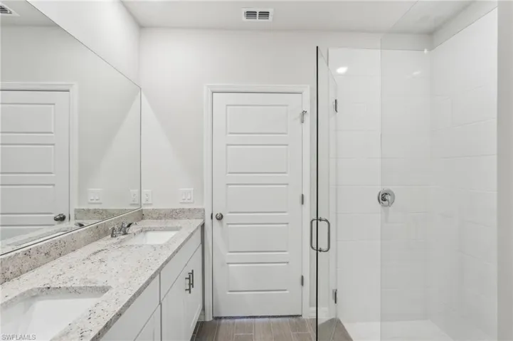 Bathroom featuring a shower stall, double vanity, a sink, and visible vents