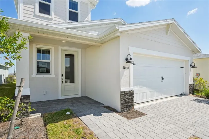 Doorway to property with decorative driveway, stone siding, a garage, and stucco siding