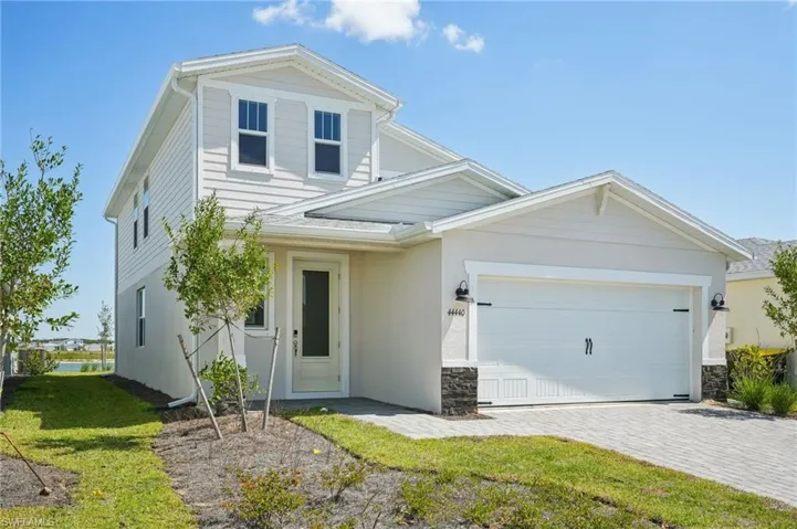 Traditional home with an attached garage, stone siding, decorative driveway, and stucco siding