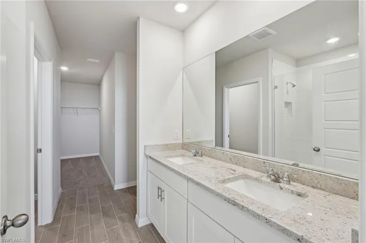 Full bathroom featuring tiled shower, a sink, a spacious closet, and visible vents