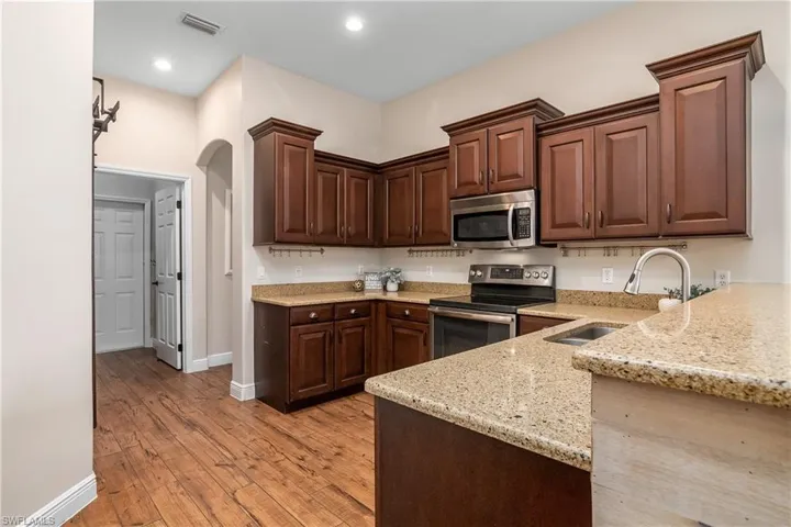 Kitchen featuring granite countertops, plank tile flooring, kitchen peninsula, sink, and appliances with stainless steel finishes