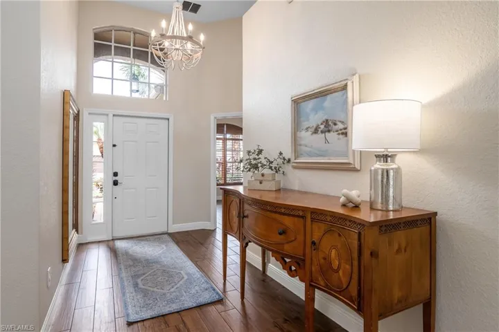 Entrance foyer featuring wood-type flooring, a towering ceiling, plenty of natural light, and an inviting chandelier