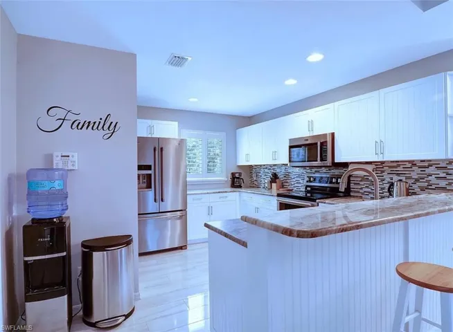 Kitchen featuring white cabinets, kitchen peninsula, stainless steel appliances, a breakfast bar area, and decorative backsplash