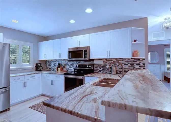 Kitchen featuring appliances with stainless steel finishes, white cabinetry, kitchen peninsula, light stone countertops, and sink