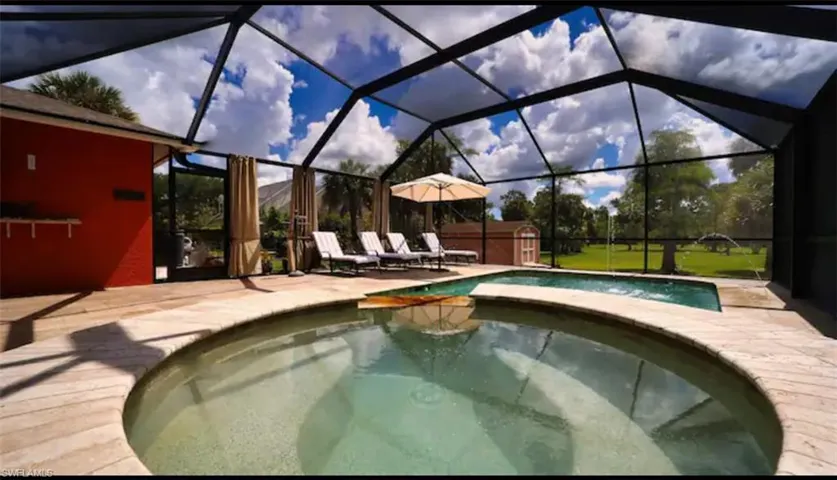 View of swimming pool featuring glass enclosure, an in ground hot tub, and a patio area