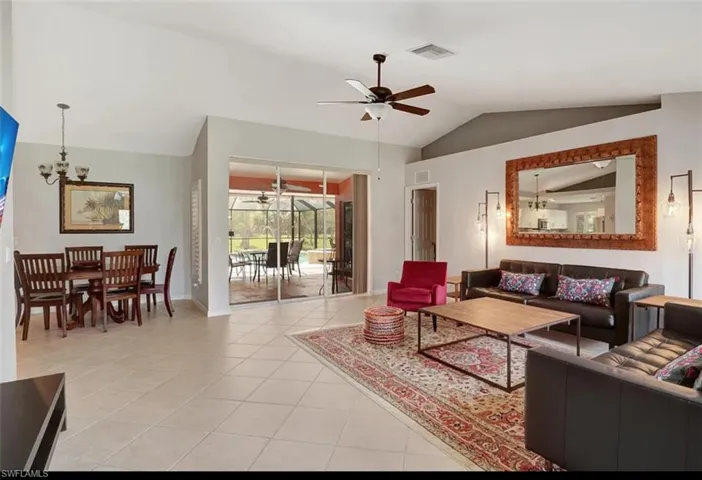Living room featuring ceiling fan with notable chandelier, lofted ceiling, and light tile patterned floors