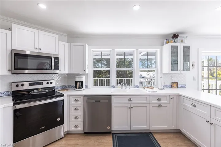 Kitchen with tasteful backsplash, a sink, light countertops, stainless steel appliances, and white cabinetry