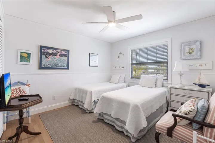 Bedroom with ceiling fan, ornamental molding, wood finished floors, and a wainscoted wall