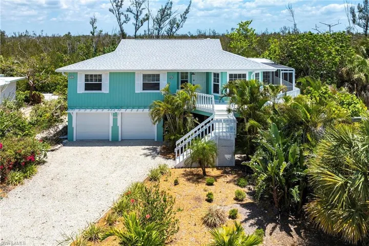 Beach home featuring covered porch, roof with shingles, an attached garage, driveway, and stairway