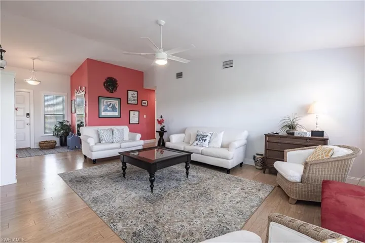 Living room with visible vents, a ceiling fan, wood finished floors, and vaulted ceiling