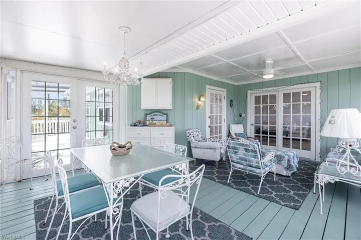Dining room with french doors, wood walls, wood finished floors, beamed ceiling, and ceiling fan with notable chandelier