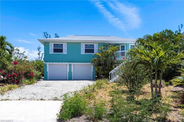 Coastal home featuring stairs, an attached garage, and driveway