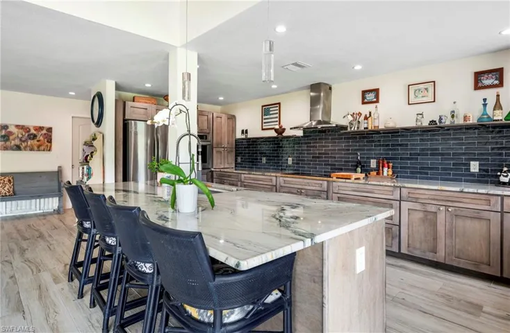 Kitchen with a breakfast bar, light stone countertops, backsplash, a spacious island, and light wood-type flooring