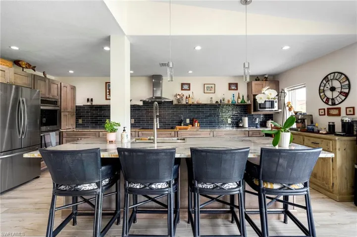 Kitchen featuring stainless steel appliances, light stone countertops, a large island with sink, pendant lighting, and tasteful backsplash