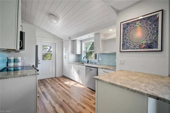 Kitchen featuring sink, stainless steel appliances, light stone counters, vaulted ceiling, and light wood-type flooring