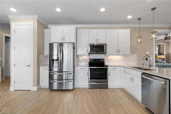 Kitchen with white cabinetry, stainless steel appliances, crown molding, decorative light fixtures, and sink