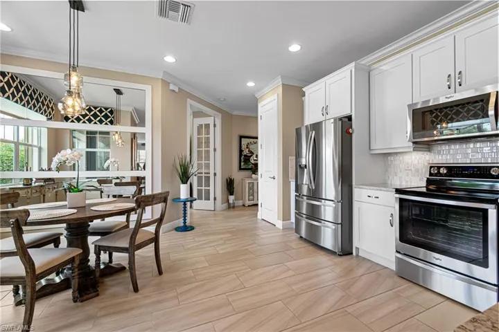 Kitchen with pendant lighting, white cabinets, decorative backsplash, appliances with stainless steel finishes, and crown molding