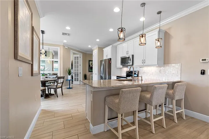 Kitchen with a kitchen breakfast bar, light stone counters, white cabinets, pendant lighting, and stainless steel appliances