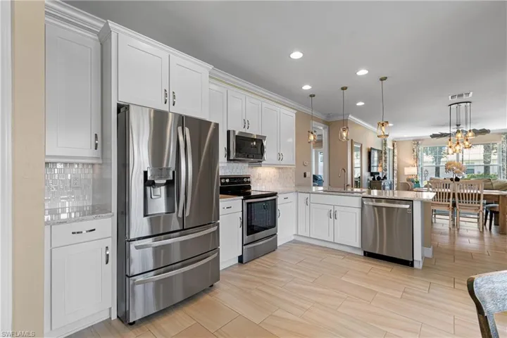 Kitchen with pendant lighting, sink, kitchen peninsula, white cabinetry, and stainless steel appliances
