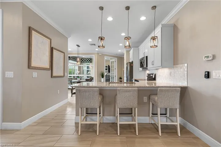 Kitchen with white cabinets, pendant lighting, appliances with stainless steel finishes, a breakfast bar area, and light stone countertops