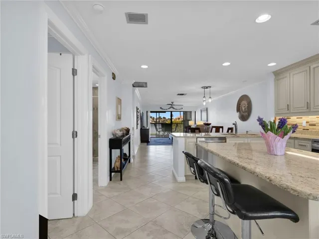 Kitchen featuring crown molding, a breakfast bar area, pendant lighting, open floor plan, and light stone counters