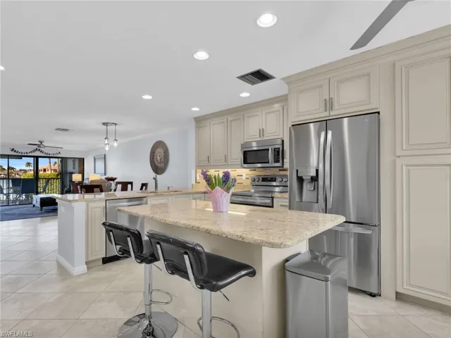 Kitchen featuring ceiling fan, a breakfast bar area, appliances with stainless steel finishes, light stone countertops, and ornamental molding