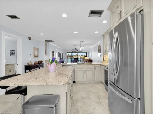 Kitchen with stainless steel appliances, crown molding, open floor plan, light stone countertops, and a peninsula