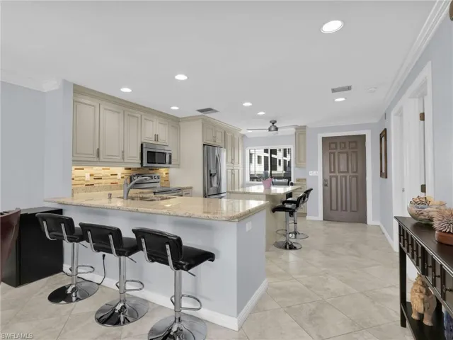 Kitchen with a breakfast bar area, crown molding, cream cabinetry, light stone counters, and a peninsula
