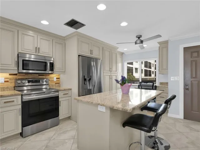 Kitchen with cream cabinets, appliances with stainless steel finishes, light stone countertops, decorative backsplash, and recessed lighting